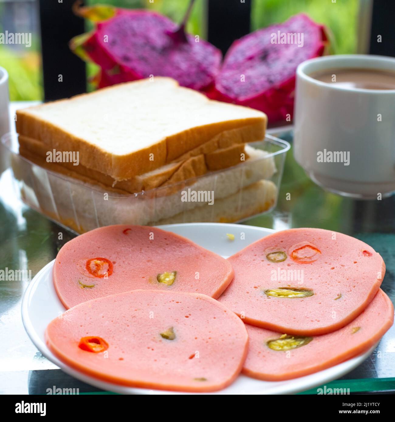Frühstück auf dem Balkon. Wurstaufschnitt mit Pfeffer, einer Tasse Kaffee, Brot und Obst. Stockfoto