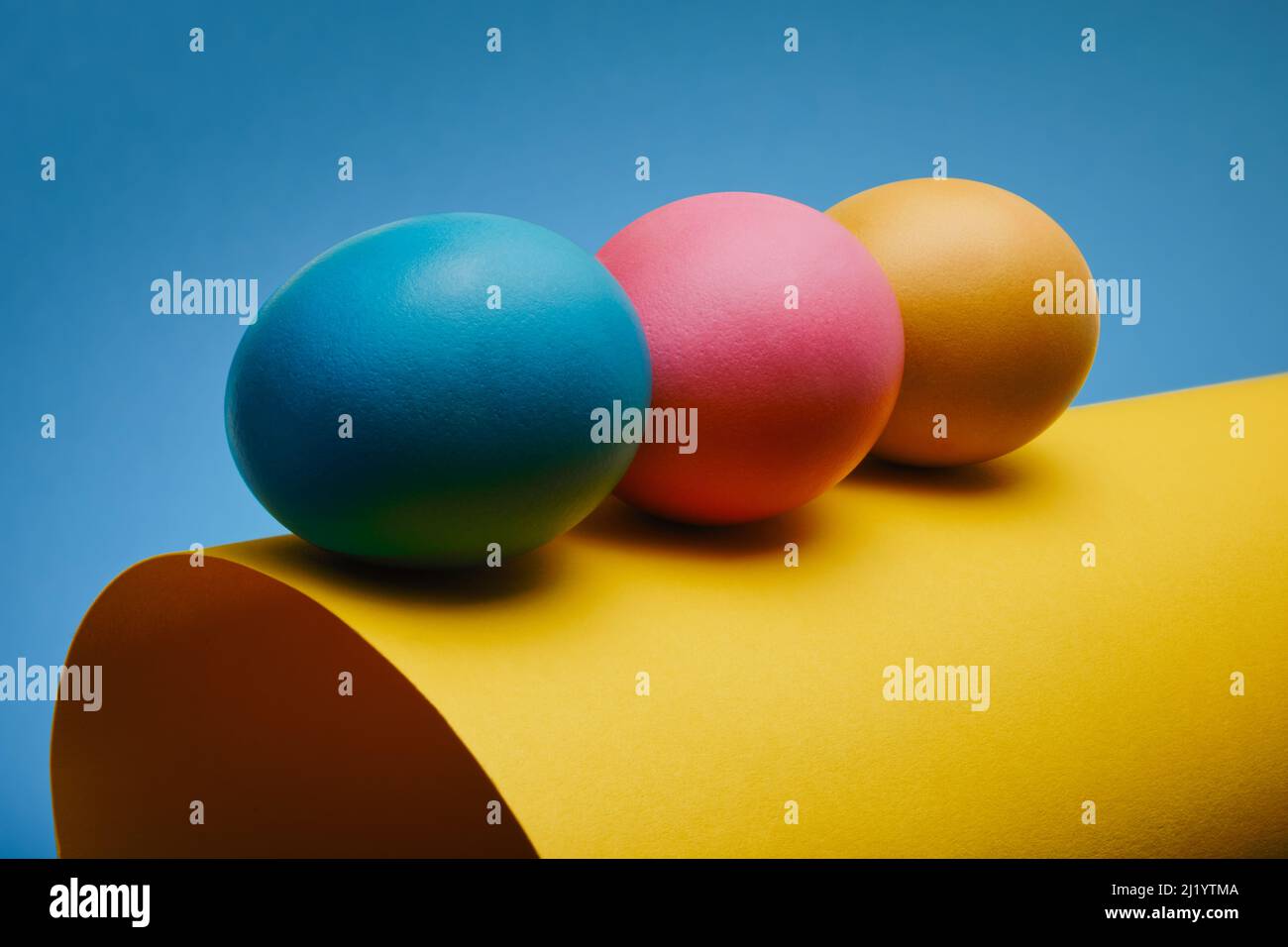 Bunte drei Ostereier auf einem gerollten Blatt Papier vor blauem Hintergrund Stockfoto