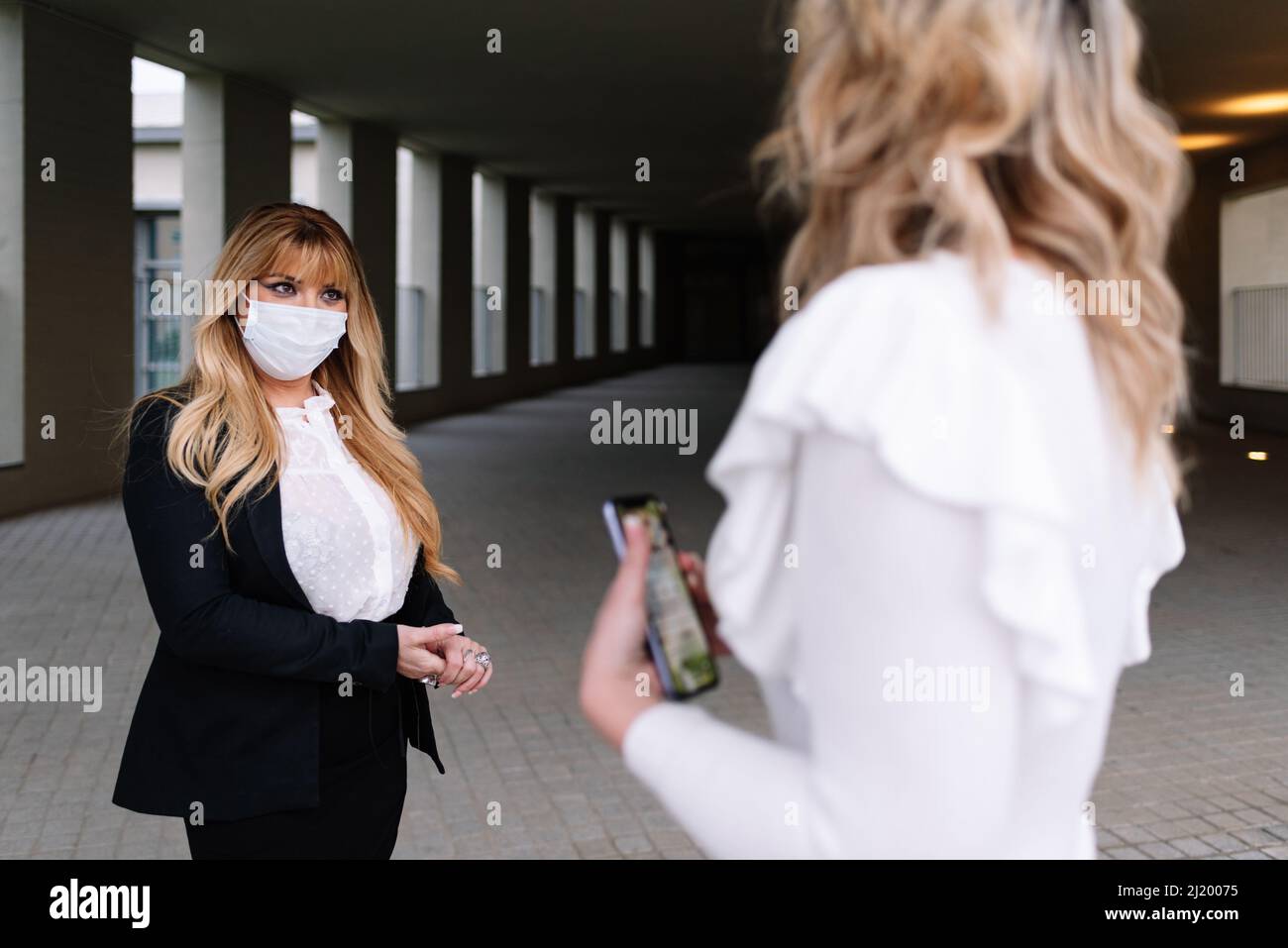 Zwei Frauen, die Masken tragen, halten während der Pandemie des Covid-19-Coronavirus einen sicheren Abstand ein, während sie auf der Straße sprechen. Sicherheitskonzept. Stockfoto