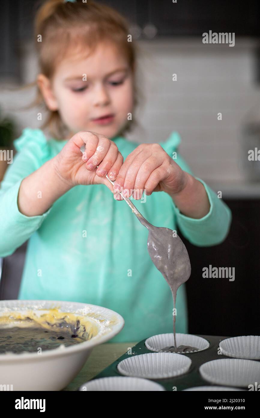 Kinder machen Muffins in der Küche. Kleines Mädchen, das zu Hause kocht. Kind lernt zu kochen, Kuchen backen, ihrer Mutter zu Hause helfen Stockfoto