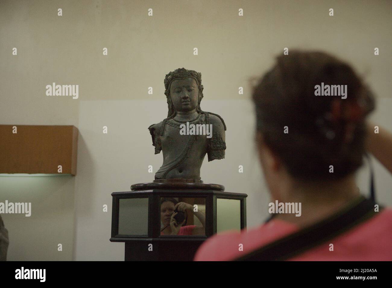 Ein Besucher fotografiert eine Srivijaya-Skulptur von Bodhisattva Avalokiteswara aus der Srivijaya-Zeit im Nationalmuseum, Bangkok, Thailand. Die ikonische Skulptur, die in der Provinz Surat Thani im Süden Thailands gefunden wurde, ist in Form von Repliken in Chaiya, einer Stadt in derselben Provinz, so vertraut. Es wird angenommen, dass 'Chaiya' von 'Srivijaya' oder 'Siwichai' ('Sivichai') im lokalen Dialekt abgeleitet wird. Stockfoto