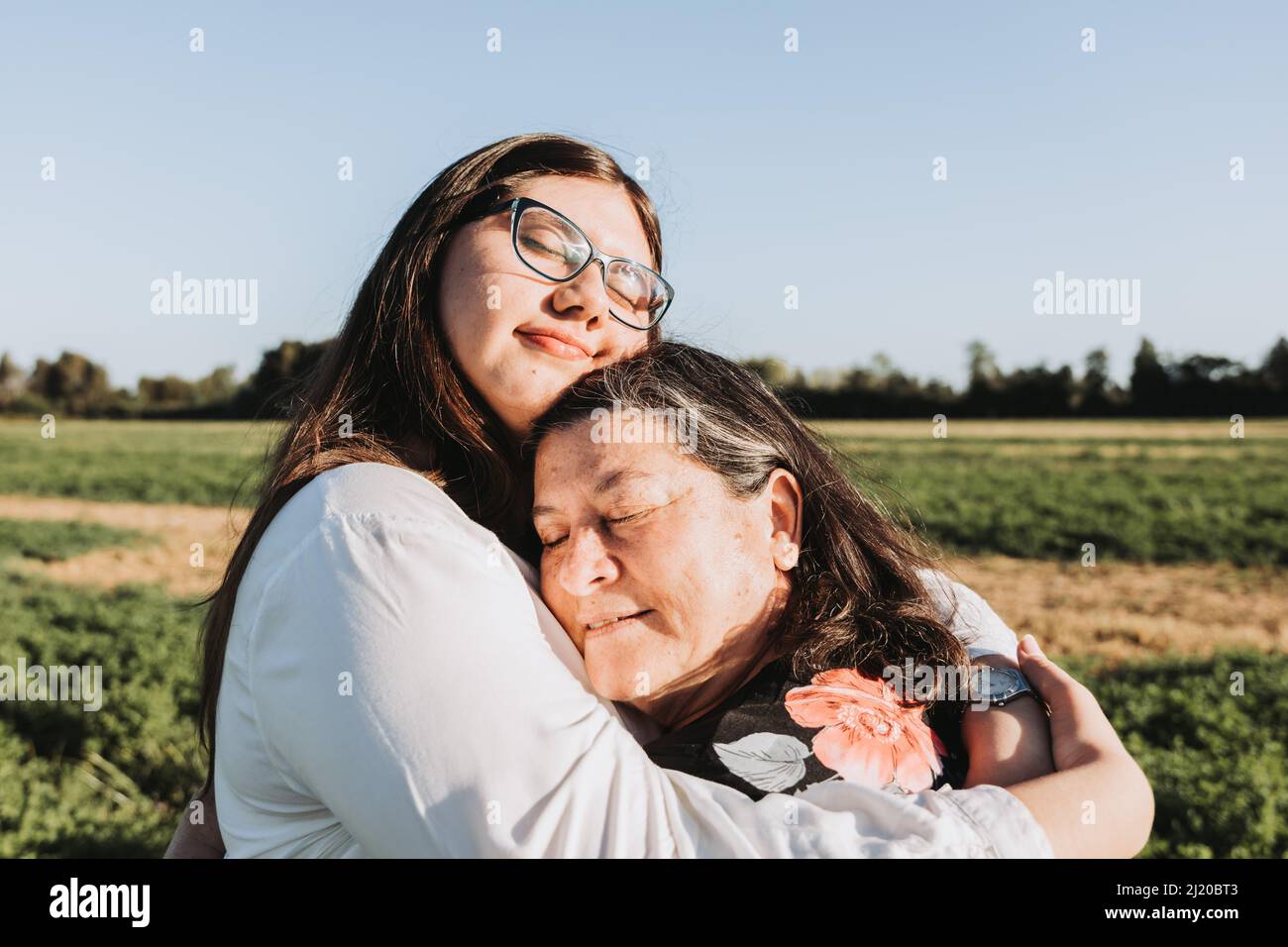 Großmutter und Enkelin umarmen sich an einem sonnigen Nachmittag mitten auf dem Feld. Familienportrait. Stockfoto