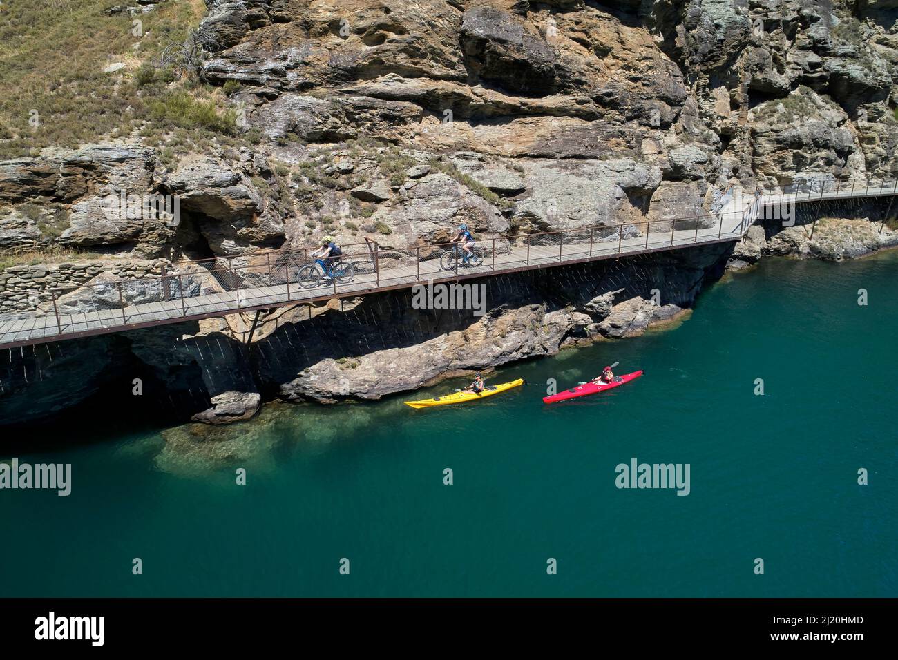 Radfahrer auf der Freischwinger-Brücke auf dem Lake Dunstan Cycle Trail und Kajakfahrer, Lake Dunstan, in der Nähe von Cromwell, Central Otago, Südinsel, Neuseeland - Drohne Stockfoto