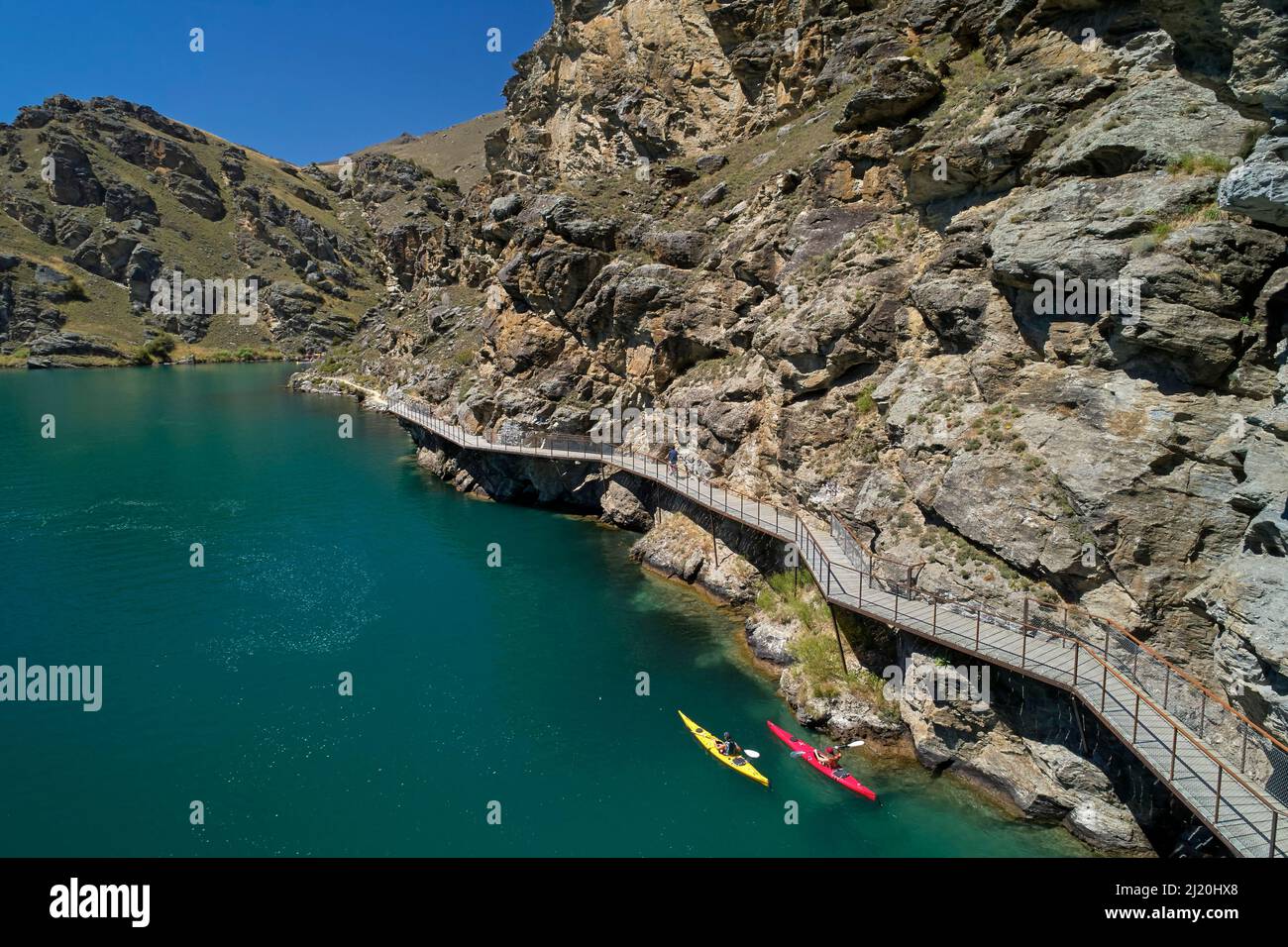 Radfahrer auf der Freischwinger-Brücke auf dem Lake Dunstan Cycle Trail und Kajakfahrer, Lake Dunstan, in der Nähe von Cromwell, Central Otago, Südinsel, Neuseeland - Drohne Stockfoto