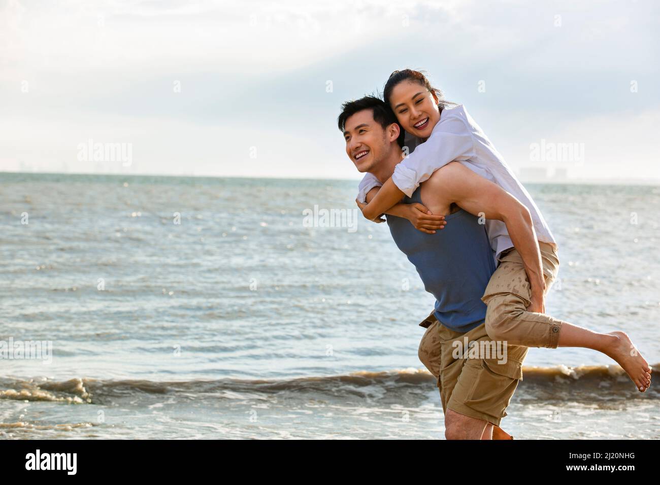 Ehemann trägt Frau auf dem Rücken an einem Sommerstrand - Stock Foto Stockfoto