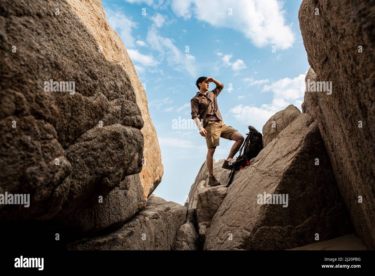 Junger männlicher Wanderer, der auf einem Strandfelsen steht und die Landschaft betrachtet - Stockfoto Stockfoto