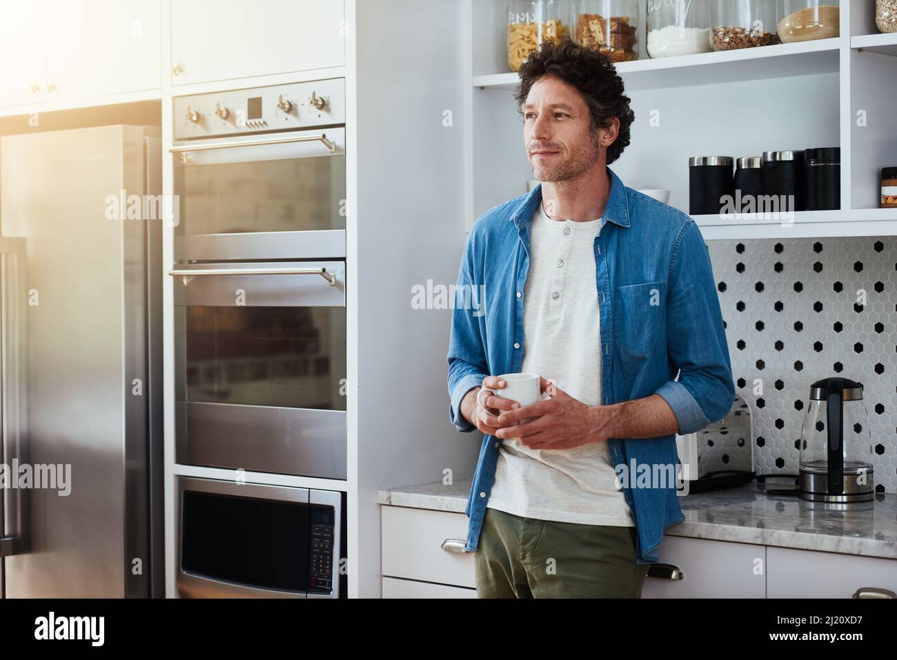 Kaffee gut genug, um sich darin zu verlaufen. Aufnahme eines Junggesellen, der sich in Kontemplation verlor, während er eine Tasse Kaffee in seiner Küche trank. Stockfoto
