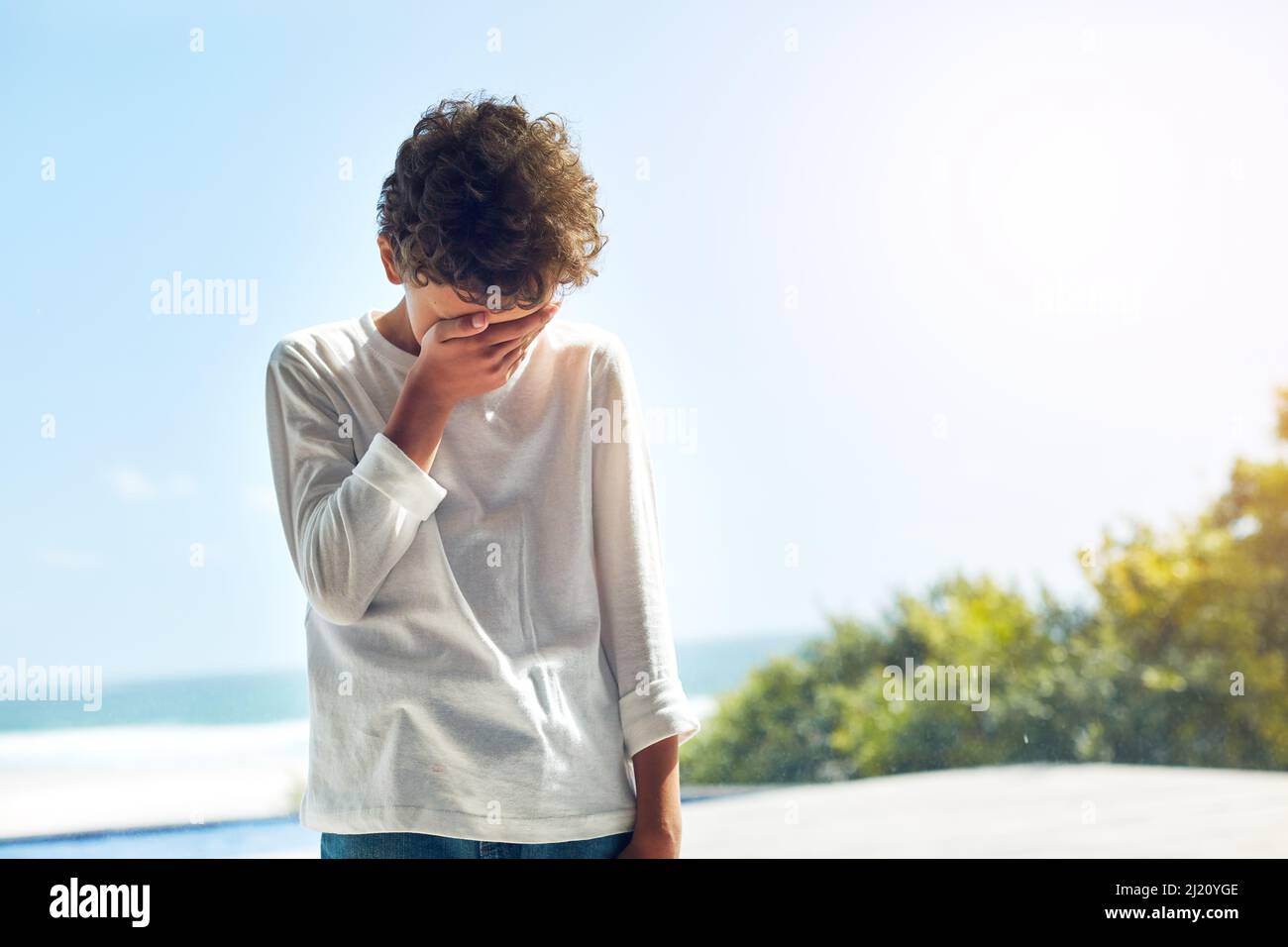 Jemand fühlt sich heute unten. Ein kurzer Schuss eines kleinen Jungen, der sein Gesicht vor Traurigkeit bedeckt. Stockfoto