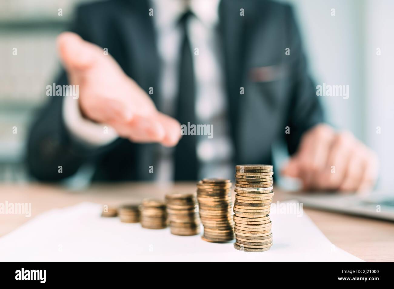 Banker, der Finanzkredite anbietet, Nahaufnahme eines Geschäftsmitleiters im Büro mit gestapelten Münzen auf dem Schreibtisch, selektiver Fokus Stockfoto