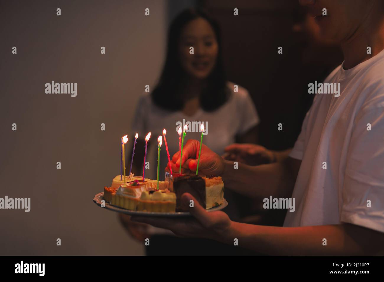 Mann hält Geburtstagskuchen mit Kerzen für Geburtstagskind im Haus. Stockfoto