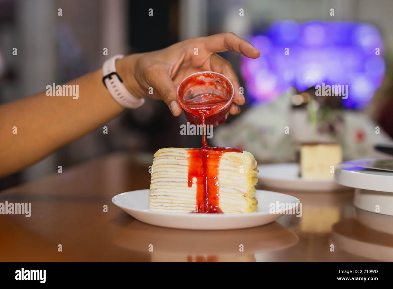 Weibliche Hand gießt Erdbeersoße über Crape Kuchen. Stockfoto