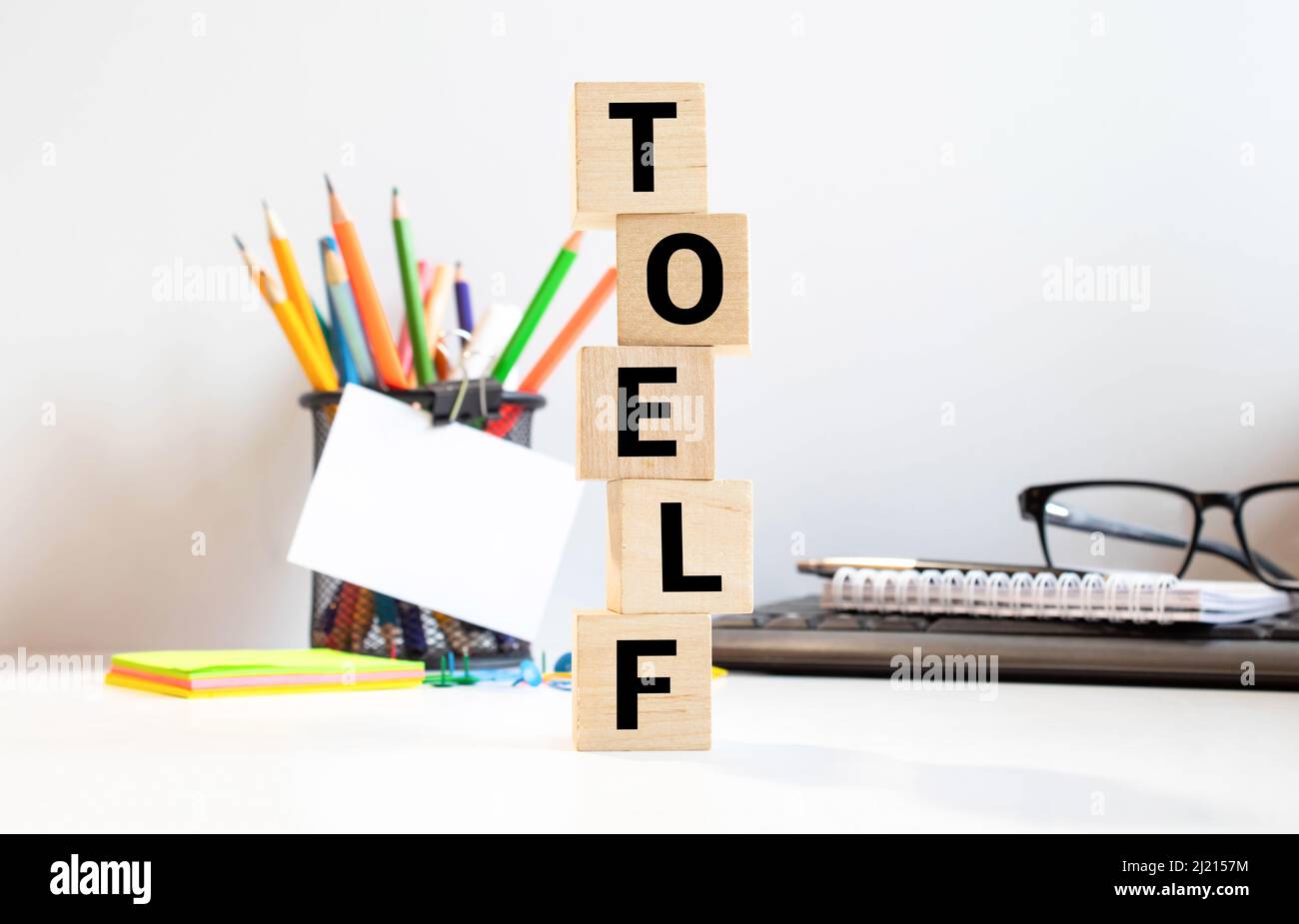 TOEFL - Wörter aus Holzblöcken mit Buchstaben, der Test des Englischen als Fremdsprache, TOEFL-Konzept, weißgrauer glänzender Hintergrund mit Reflexion Stockfoto