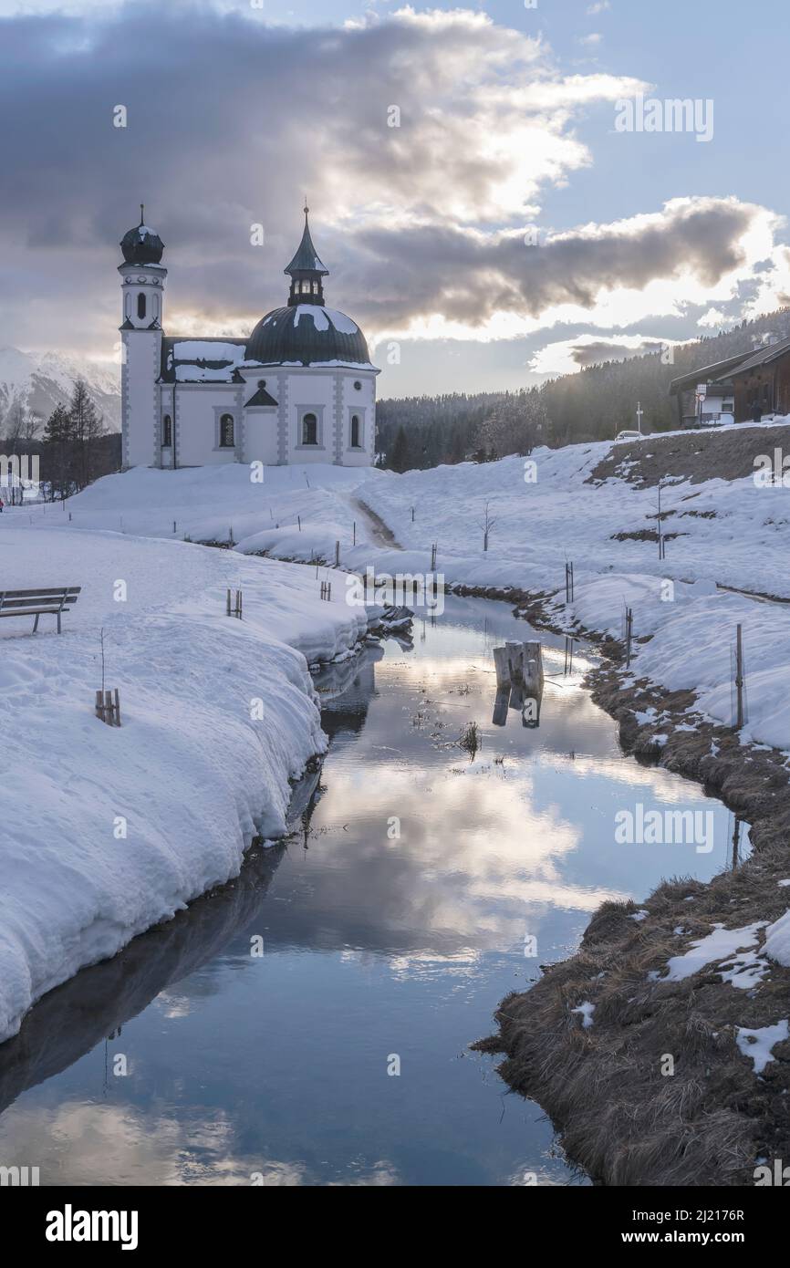 Stadtbild mit barocker Seekirchl-Kirche auf schneebedecktem Boden in touristischer Vollzeit, aufgenommen unter Sonnenuntergangswolken bei Seefeld, Tirol, Österreich, Stockfoto
