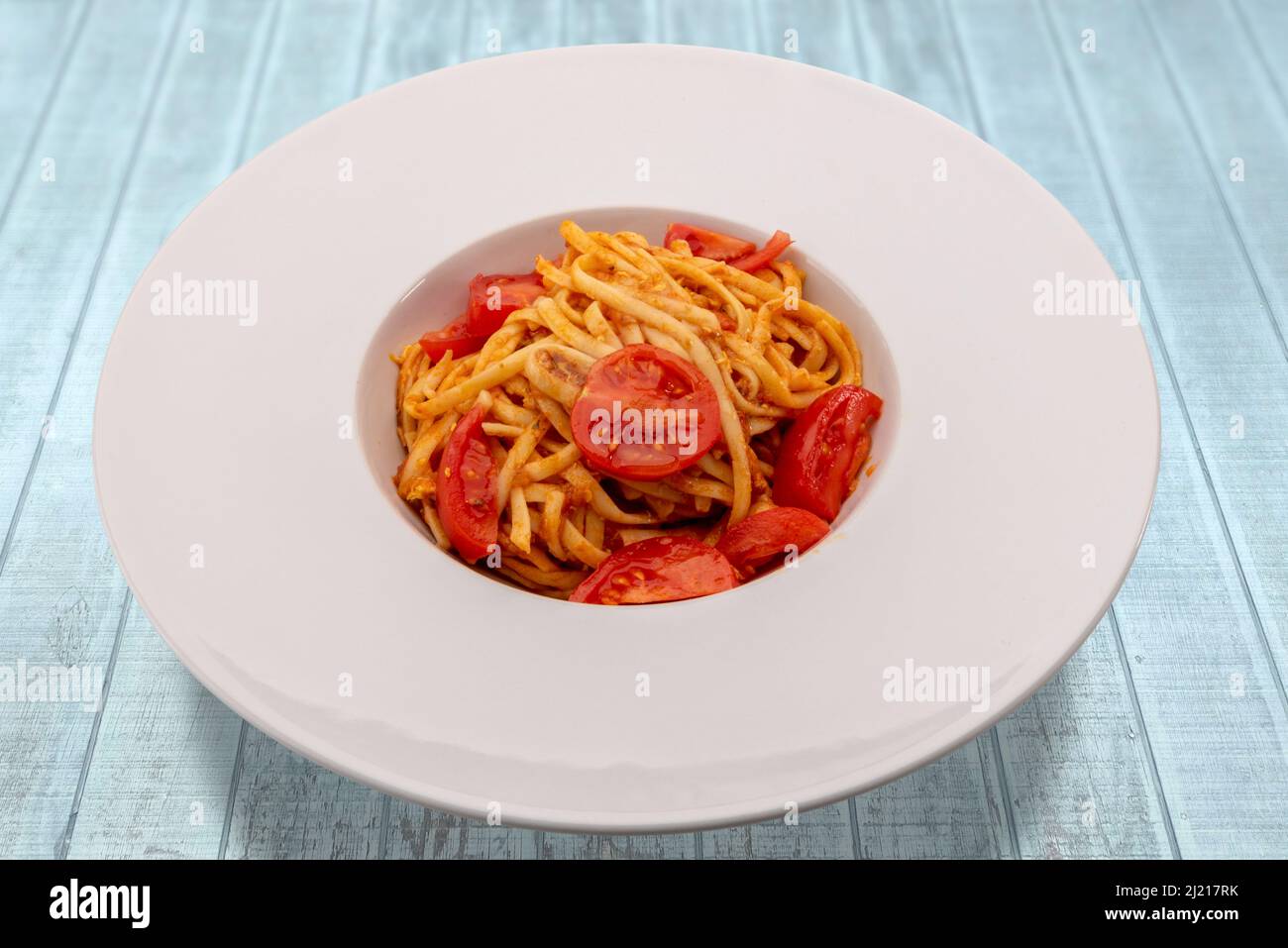 Italienische Bavette-Pasta mit Tomatensauce, Parmesan und frischen Kirschtomaten auf weißem Teller auf hellblauem Holztisch Stockfoto
