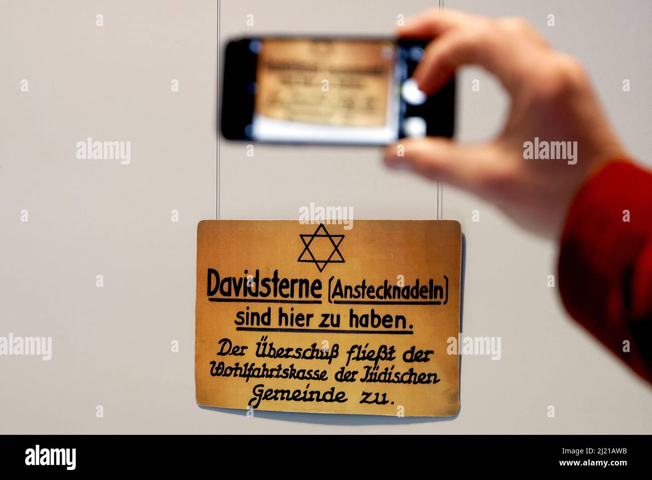 Berlin, Deutschland. 29. März 2022. Ein Mann fotografiert mit einem Handy eine Ausstellung, die in der Ausstellung „Unser Mut“ lautet: „Davidsterne (Pins) sind hier erhältlich“. Juden in Europa 1945-48.' Die erste Sonderausstellung im neuen Dokumentationszentrum "Flucht, Vertreibung, Versöhnung" widmet sich jüdischen Nachkriegserfahrungen von Flucht, Vertreibung, Selbständigkeit und Wiederaufbau. Die Ausstellung ist vom 31. März bis 30. September geöffnet. Quelle: Carsten Koall/dpa/Alamy Live News Stockfoto