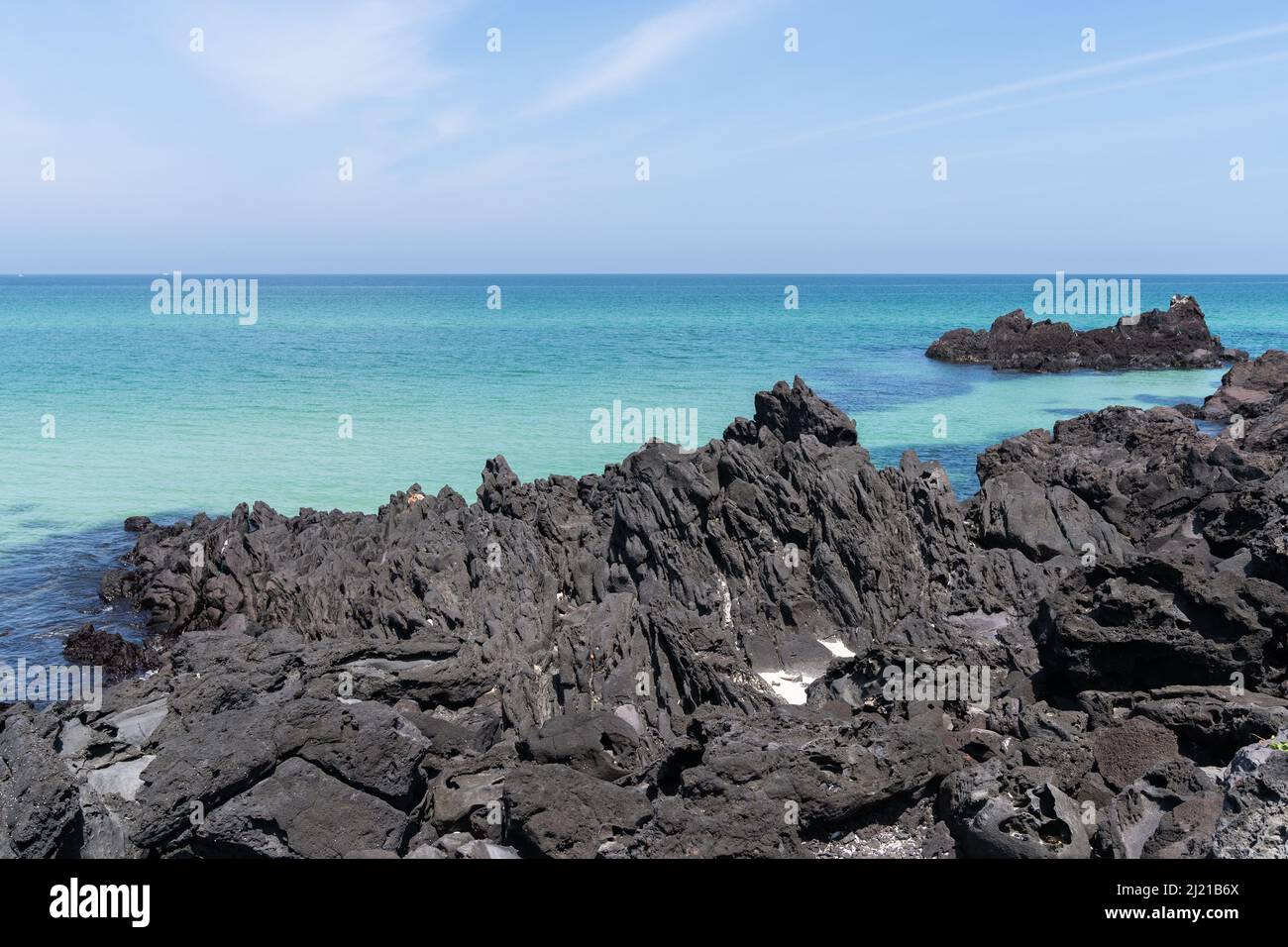Zerklüftete schwarze Vulkangesteine, die aus kristallklarem aquamarinfarbenem Wasser am Strand von Handam auf der Jeju Island, Südkorea, ragen Stockfoto