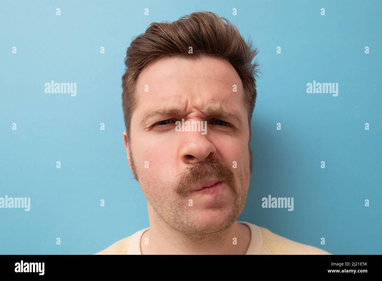 Mann mit lustigen Schnurrbart, der Zweifel hat und mit verwirrem Gesichtsausdruck auf isoliertem blauem Hintergrund Stockfoto