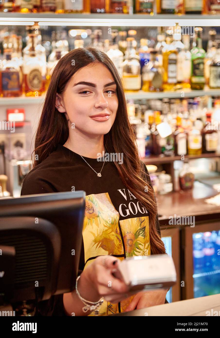 Junge Frau in Bar, die Kartenmaschine gegen Kamera/Kunde hält Stockfoto
