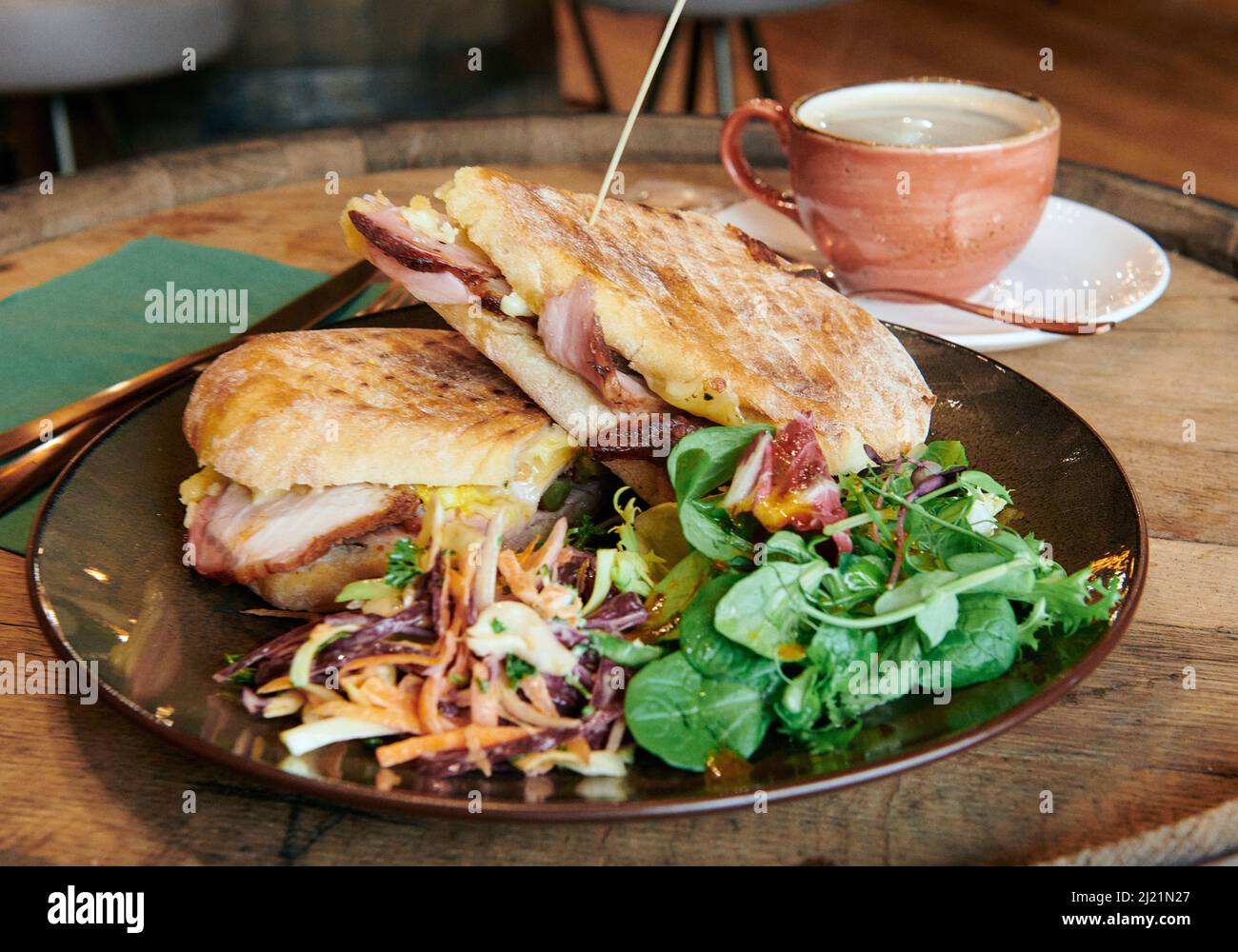 Ein geröstetes Deli-Sandwich mit einem frischen schwarzen Kaffee auf einem rustikalen Holzfass Stockfoto