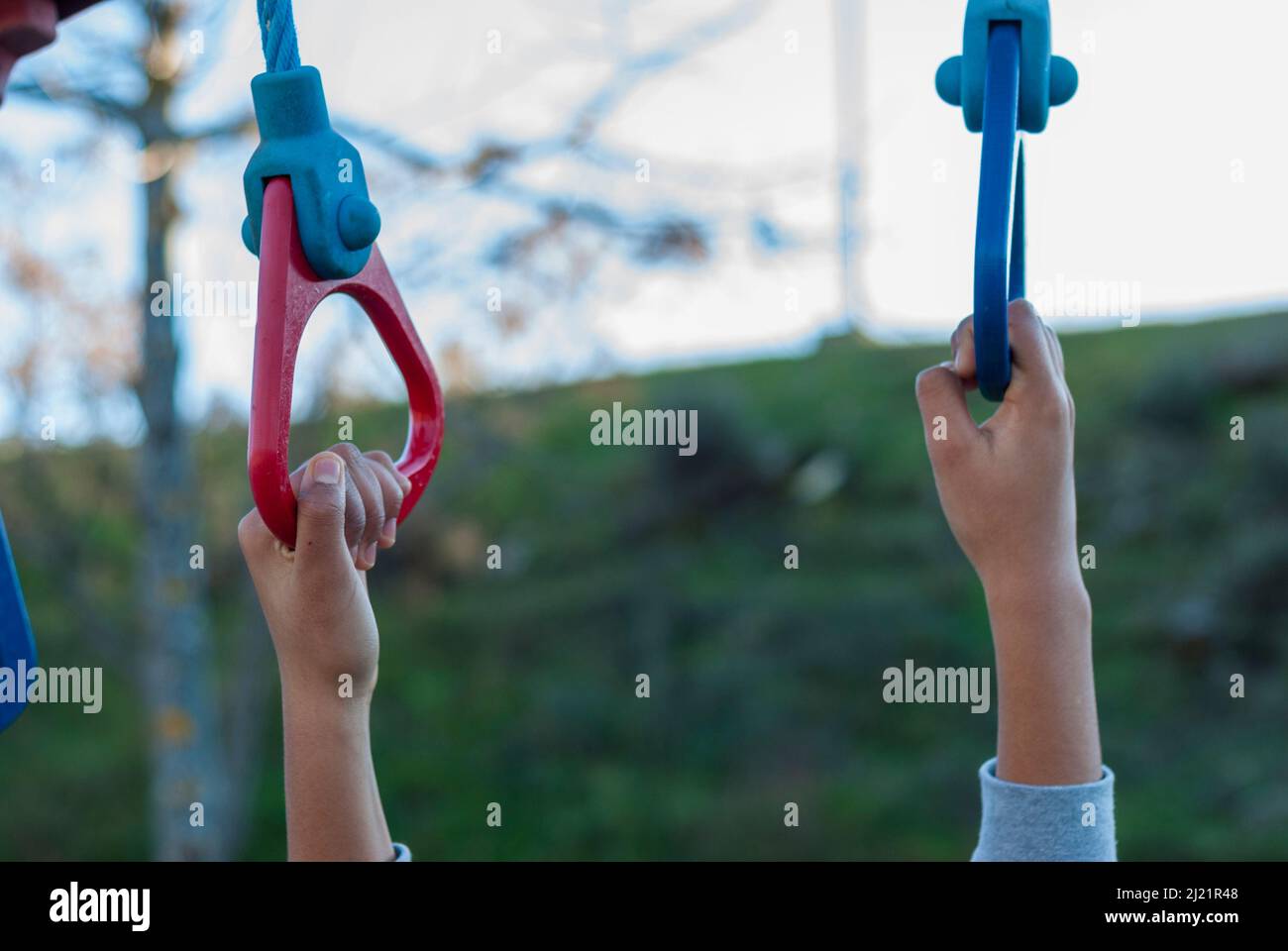 Die Hände, die sich an farbigen Ringen in einem Kinderbereich halten, sind horizontal auf dem Spielplatz im Freien Stockfoto