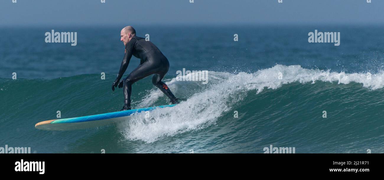 Ein Panoramabild eines männlichen Surfers, der auf einer Welle bei Fistral in Newquay in Cornwall in Großbritannien reitet. Stockfoto