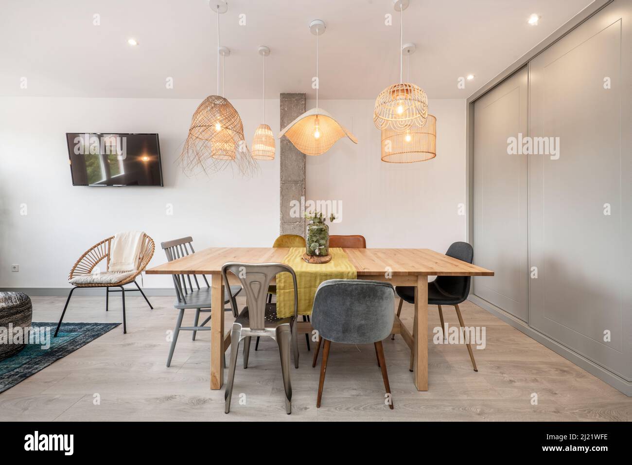 Wohnzimmer mit einem Esstisch aus Holz, gepolsterten Stühlen aus Holz und Metall und Korblampen, einem hellen Holzboden und einem Einbauschrank mit grauen en Stockfoto