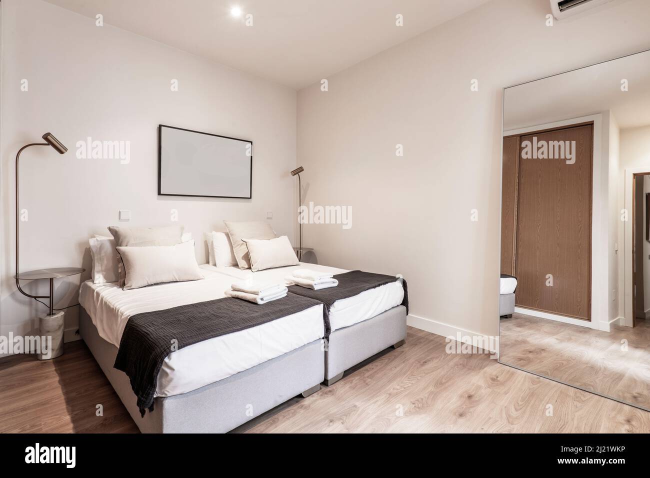 Doppelzimmer mit großem Spiegel an der Wand, weißen Kissen auf dem Bett und Beistelltischen mit Designer-Lampen Stockfoto