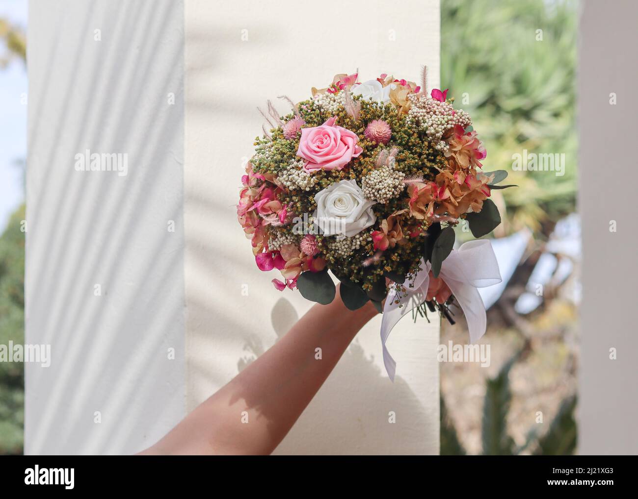 Bild von Braut Hand Halten schöne rosa Hochzeitsstrauß von Blumenhändler mit erhaltenen Blumen und getrockneten Blumen in einem Garten gemacht Stockfoto