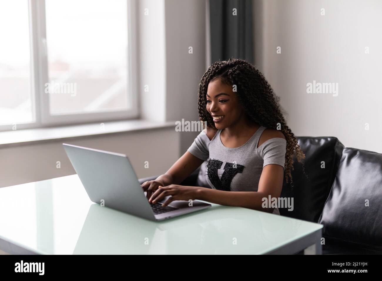 Erfolgreiche afroamerikanische junge Frau, die im modernen Büro auf dem Laptop tippt und benutzt. Geschäftskonzept Stockfoto