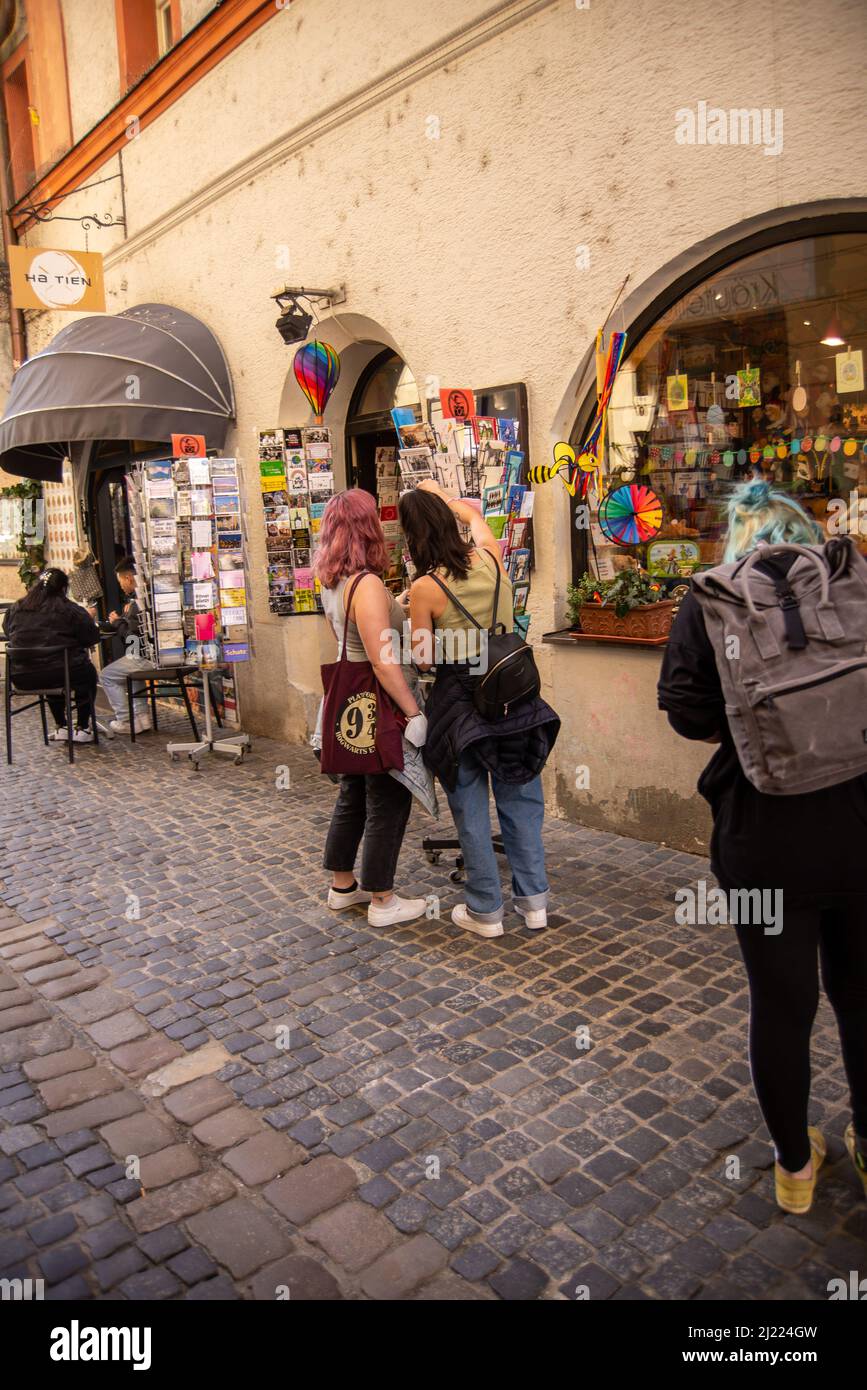 Regensburg, Deutschland-März 24,2022: Zwei junge Frauen schauen sich Postkarten vor einem Geschäft in einer Fußgängerzone an. Stockfoto