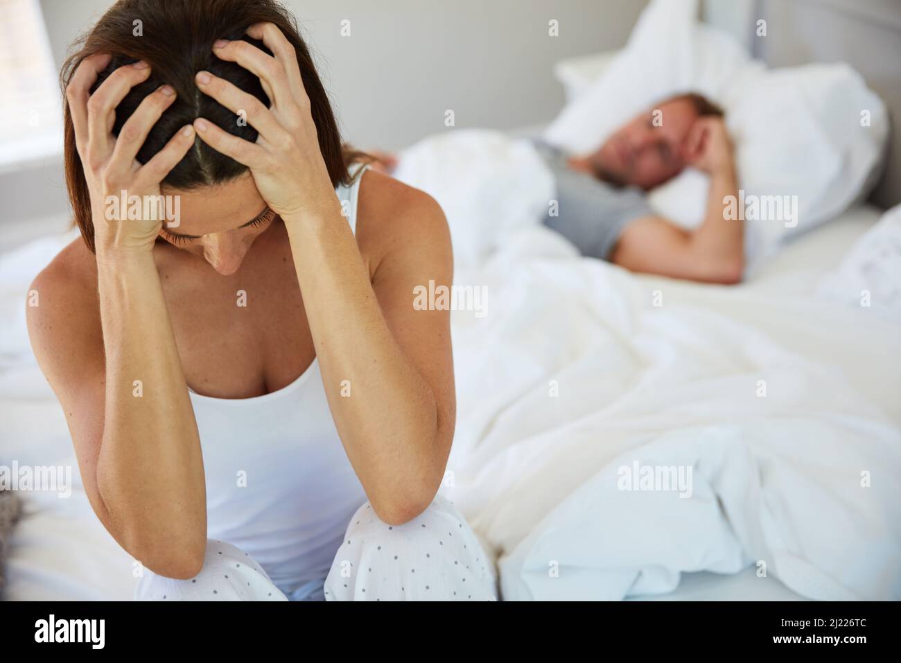 Ich habe die Nase voll von diesem ständigen Kampf. Aufnahme einer Frau, die aufgeregt aussieht, während ihr Mann im Hintergrund schläft. Stockfoto