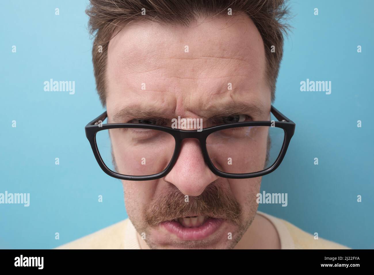Kaukasischer Mann mit Schnurrbart in großen Augen schreiend wütend und wütend. Studio auf blauer Wand. Stockfoto