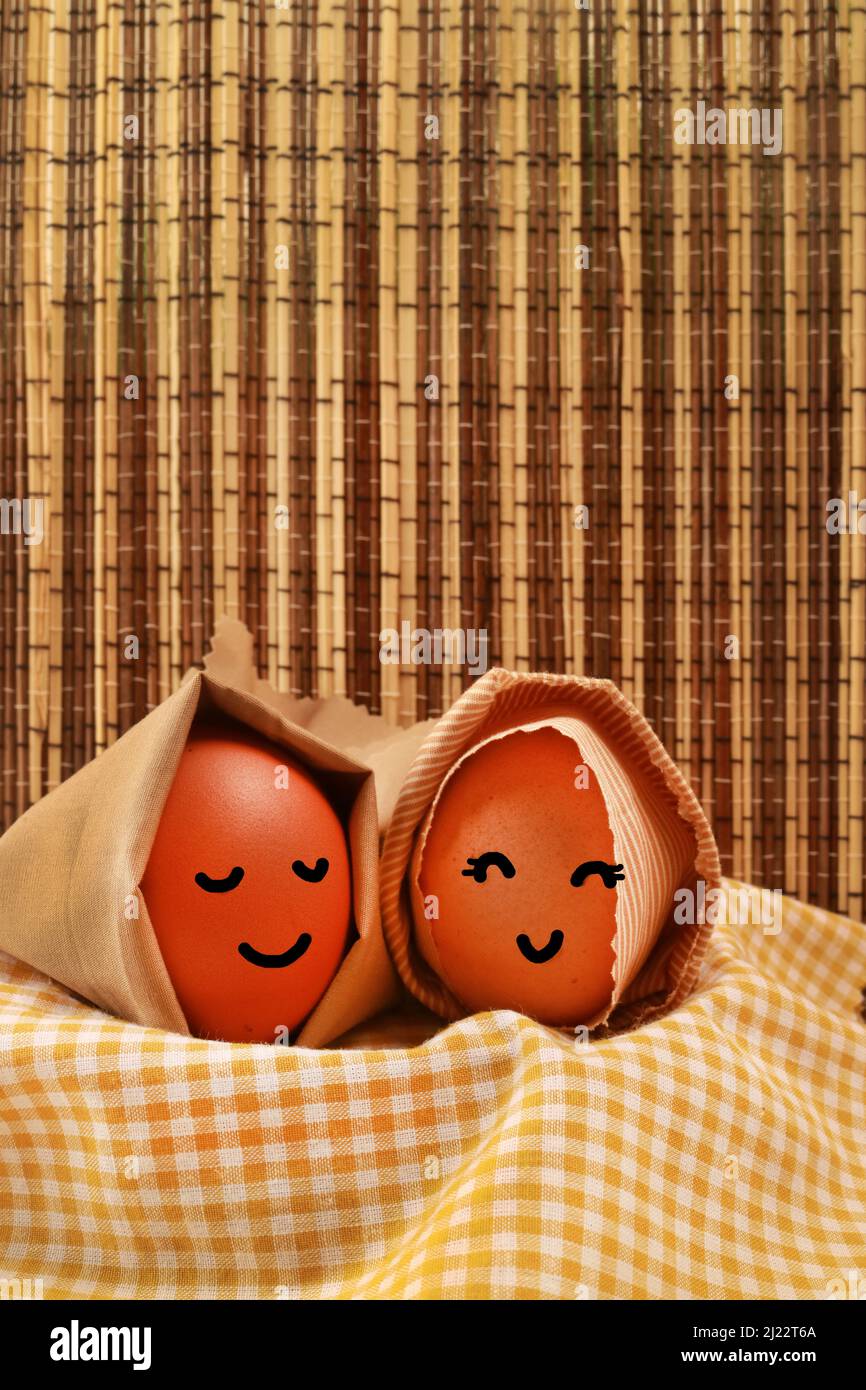 Fotostudio des Osterfeiertagskonzepts zwei Ei Kapuzen Lächeln auf gelber Serviette mit dunkelbrauner Textur Hintergrund vertikal Stockfoto