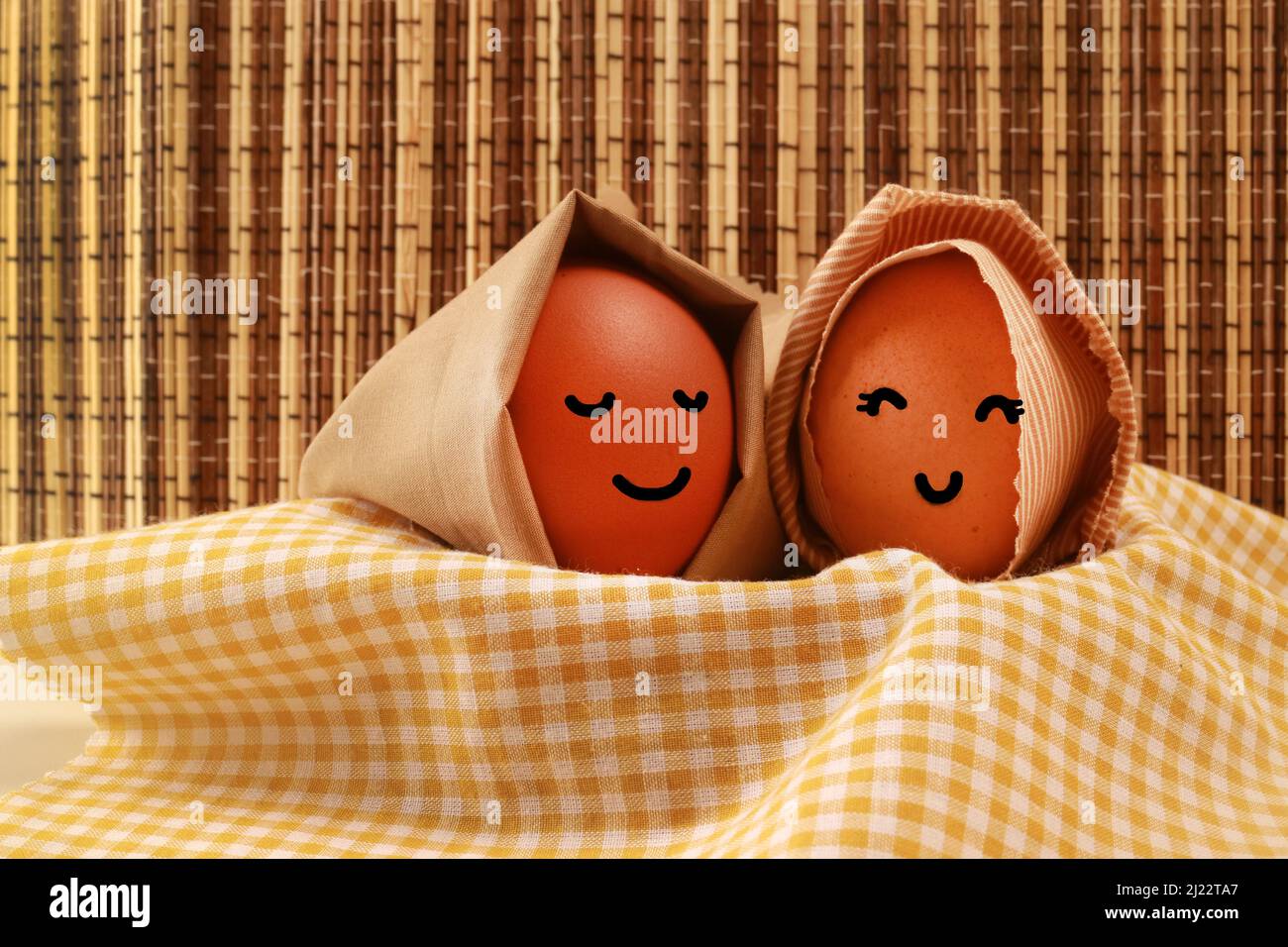 Fotostudio des Osterfeiertagskonzepts Two Egg Hooded Smile auf gelber Serviette mit dunkelbraunem Texturhintergrund Stockfoto
