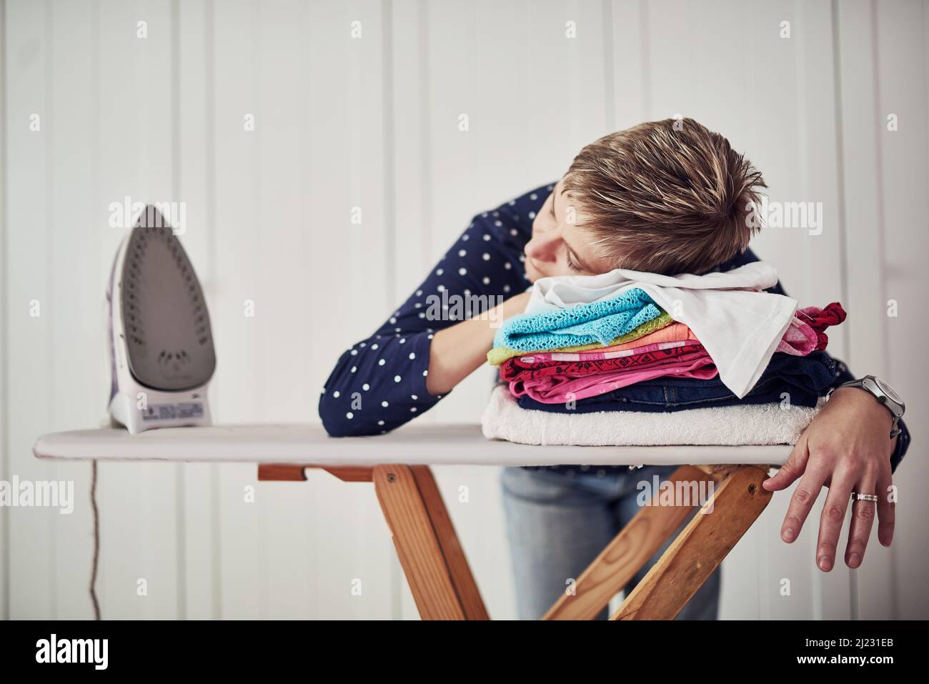 Hausarbeit ist hektisch. Aufnahme einer Frau mit dem Kopf nach unten auf einem Stapel Kleidung auf einem Bügelbrett. Stockfoto