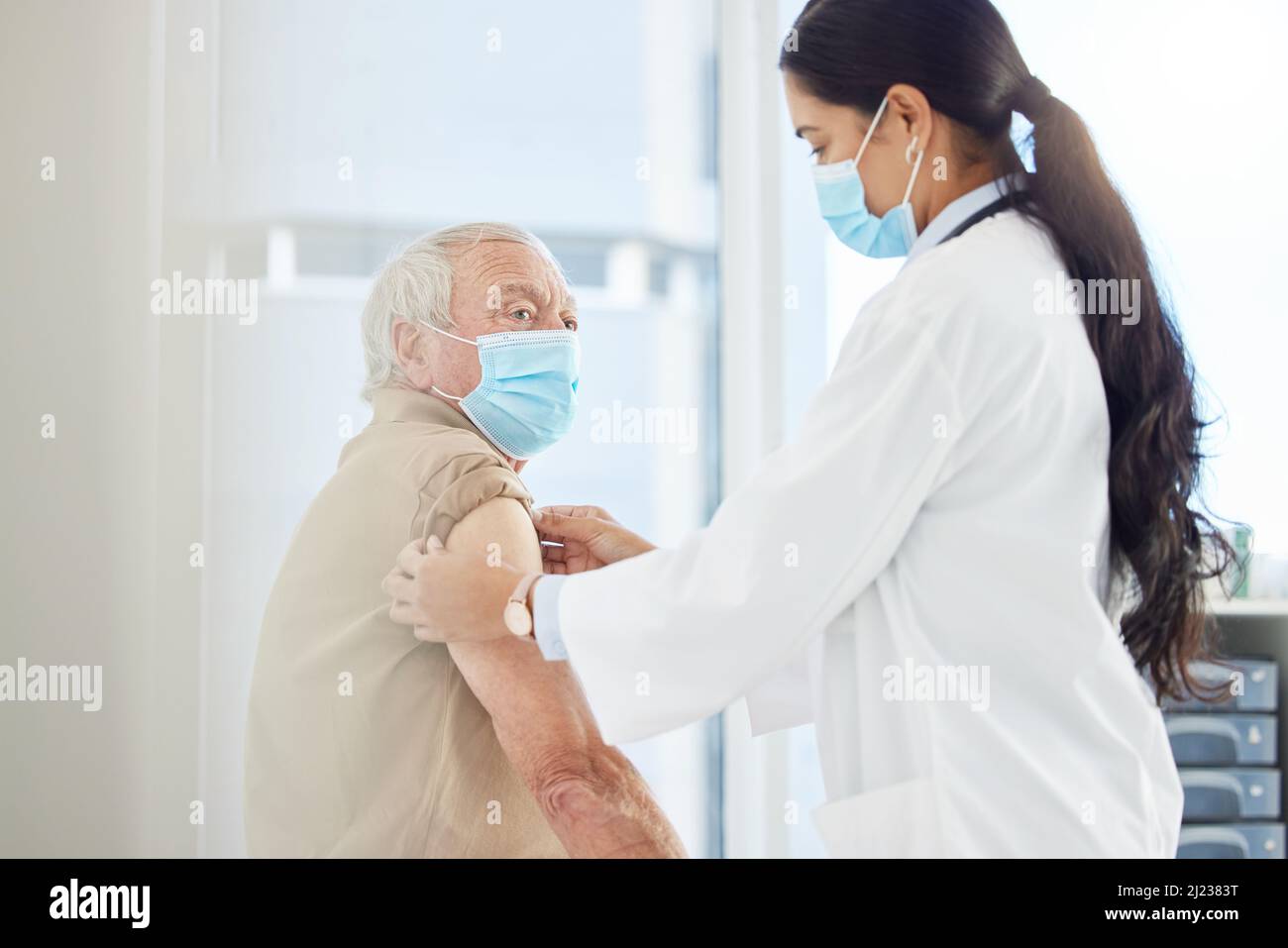 Es wird vorbei sein, bevor Sie es wissen. Aufnahme einer Ärztin mit Gesichtsmaske und Vorbereitung ihrer älteren Patientin auf einen Covid-Impfstoff in ihrer Klinik. Stockfoto