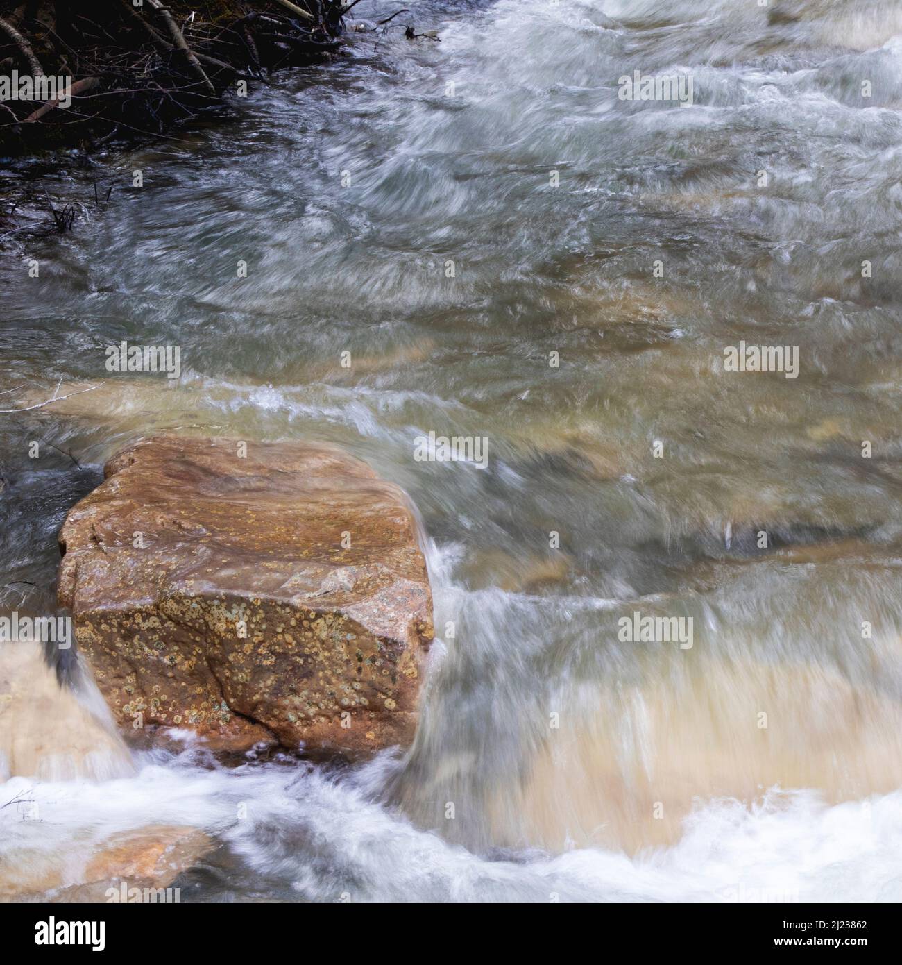 Schöner Naturstein sitzt isoliert gegen das fließende Wasser eines Baches oder Baches Stockfoto