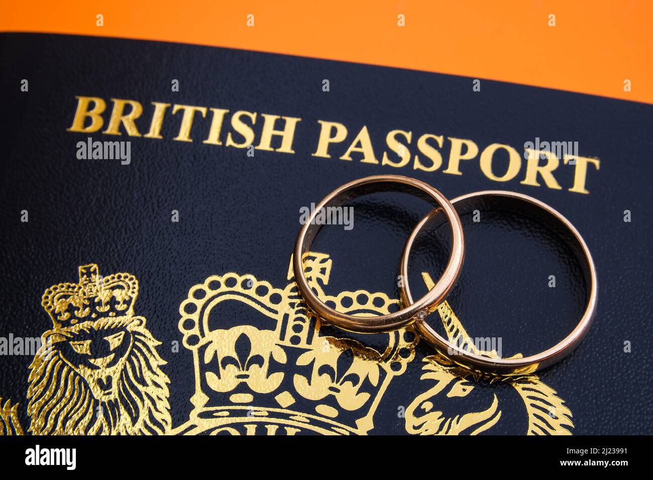Goldene Ringe auf einem neuen dunkelblauen britischen Pass. Konzept für das britische Verlobungsvisum oder das Ehepartnervisum. Stafford, Großbritannien, 29. März 2022. Stockfoto