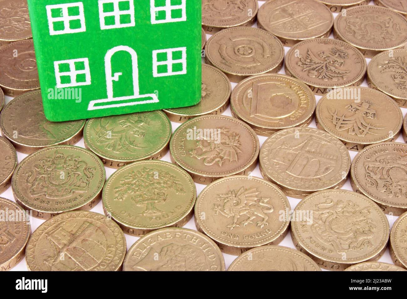 Ein grünes Haus auf einem Münzbett, eine Metapher für erneuerbare Einsparungen. Stockfoto