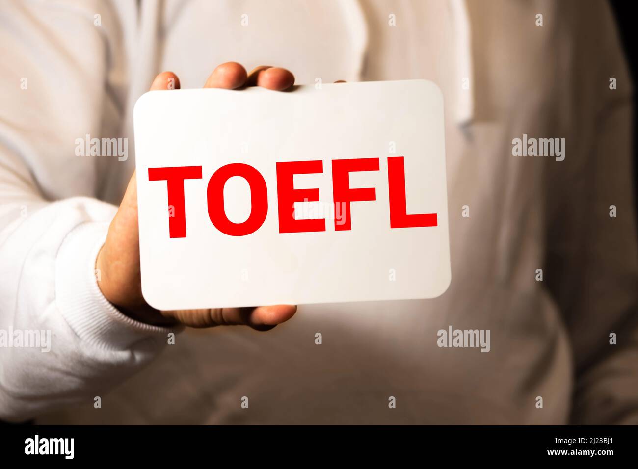 TOEFL - Test of English as a Foreign Language. Text auf weißem Papier auf hellweißem Hintergrund. Im Hintergrund ist eine Lupe, ein Diagramm, eine Kalk Stockfoto