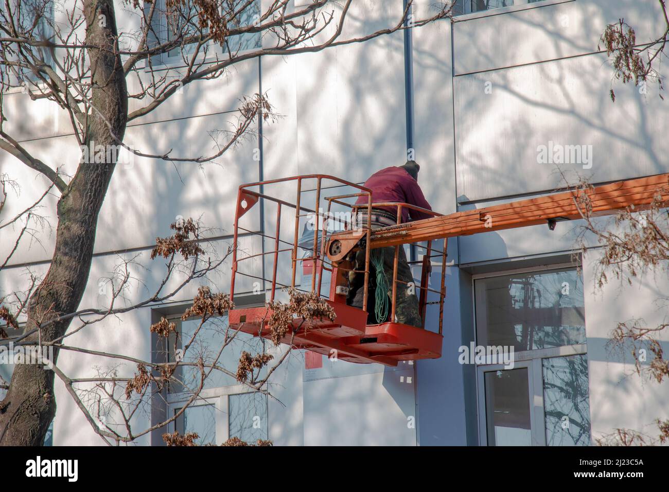 Der Bauherr in einem Krankorb repariert die Beschichtung einer Metallstruktur an der Wand der Fassade eines Gebäudes. Stockfoto