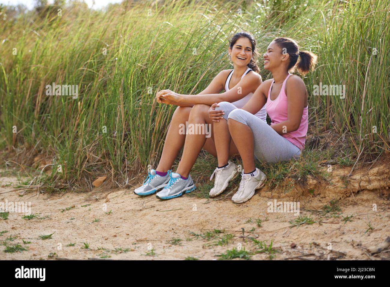 Einen Witz mit Freunden teilen. Zwei Freunde sitzen draußen und lachen zusammen, während sie Übungskleidung tragen. Stockfoto