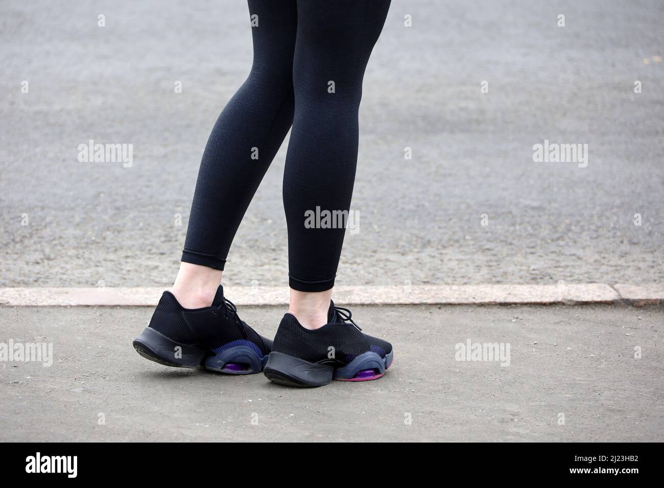 Weibliche Beine in Turnschuhen und Leggings auf Asphalt, schlanke Läuferin auf einer Straße. Konzept des Frühjahrstraining in der Stadt Stockfoto