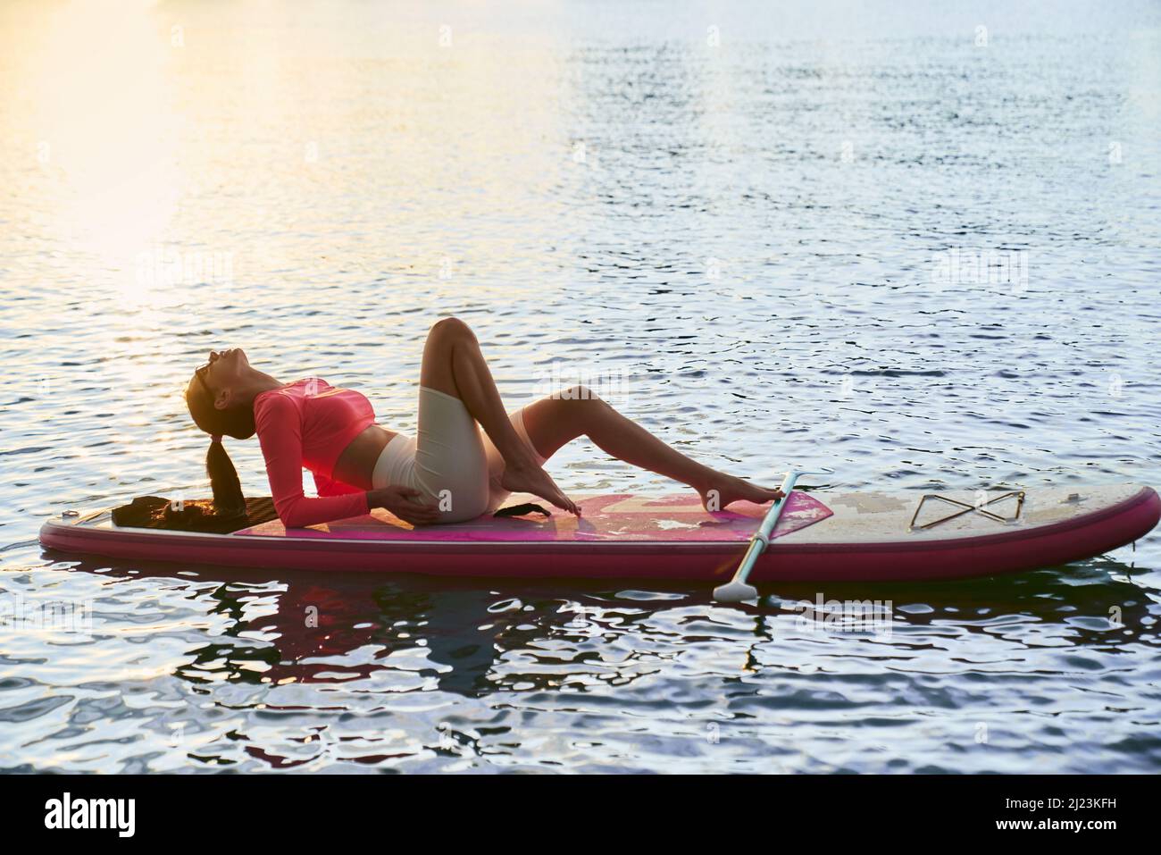 Attraktive kaukasische Frau mit schlanken liegend auf dem Brett während der Pause während des Outdoor-Training. Wassersport und gesunde Lebensweise Konzept. Stockfoto