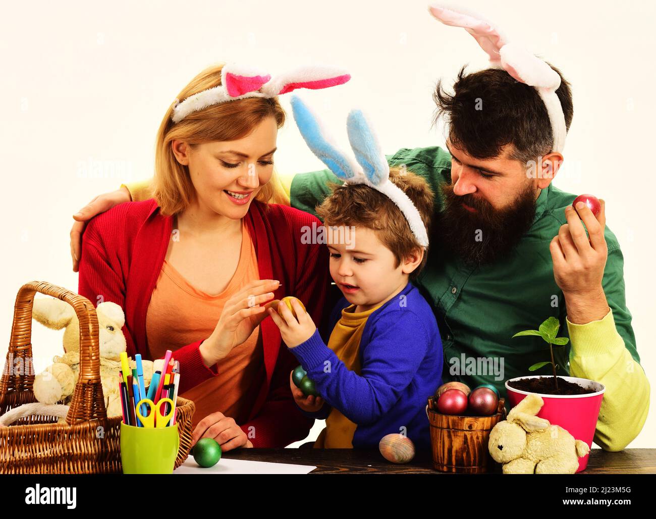 Traditionen der Osterfamilie. Eltern und Kind in Hasenohren mit bunten Eiern, die sich auf den Urlaub vorbereiten. Stockfoto