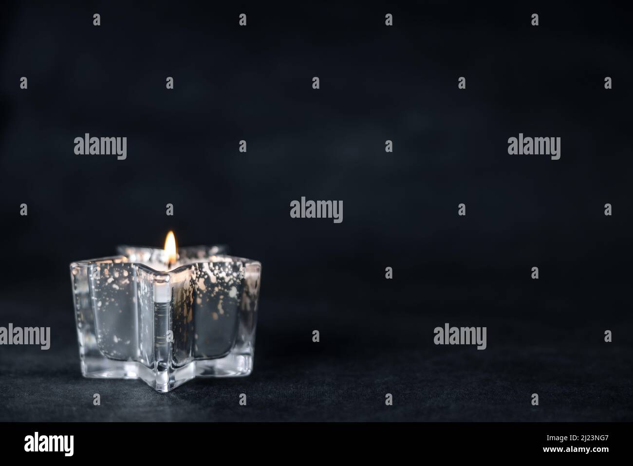 Ein marineblauer und friedlicher Hintergrund mit viel Platz für Kopien und einer brennenden sternförmigen Kerze aus Quecksilberglas Stockfoto