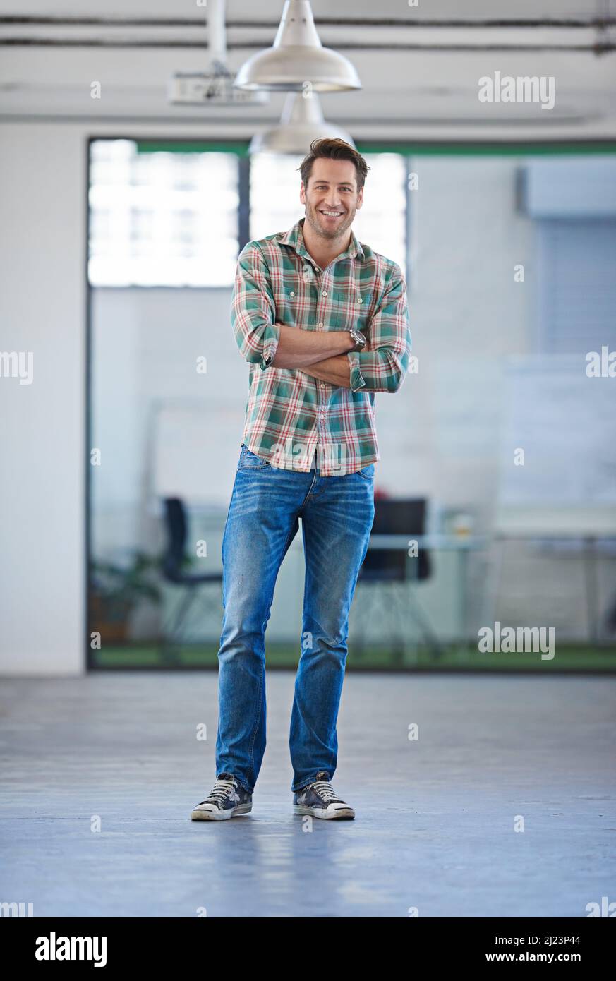 Gesicht der modernen Führung. Gutaussehender Mann, der in einer offenen Industriefläche in informeller Kleidung steht und positiv aussieht. Stockfoto
