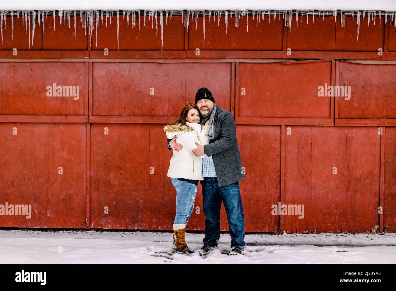 Mann und Frau umarmen sich vor der Roten Holzwand und den Eiszapfen Stockfoto