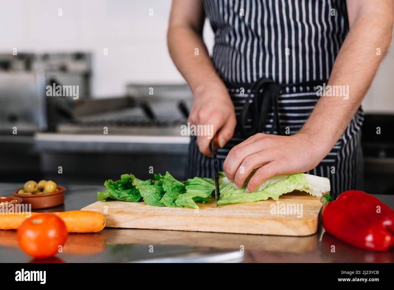 Detail der Hände eines jungen männlichen Chefs, der in einer professionellen Küche Lebensmittel schneidet Stockfoto