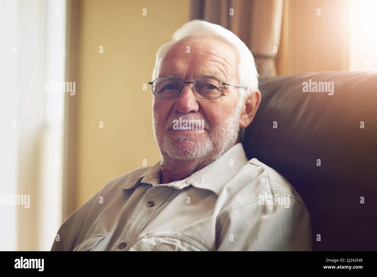 Ich bin mit dem Älterwerden zufrieden. Beschnittenes Porträt eines glücklichen älteren Mannes, der sich zu Hause auf dem Sofa entspannt. Stockfoto